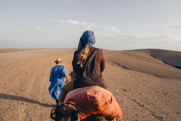 Two people riding camels through a desert landscape.